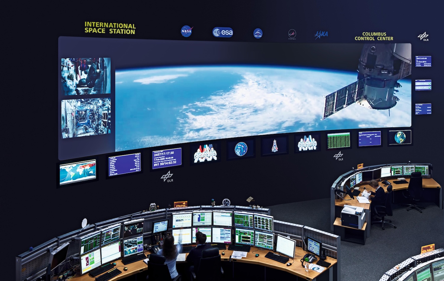 Ein großer Bildschirm im Kontrollzentrum Oberpfaffenhofen zeigt einen Satelliten in einer Umlaufbahn, darunter die Erde.