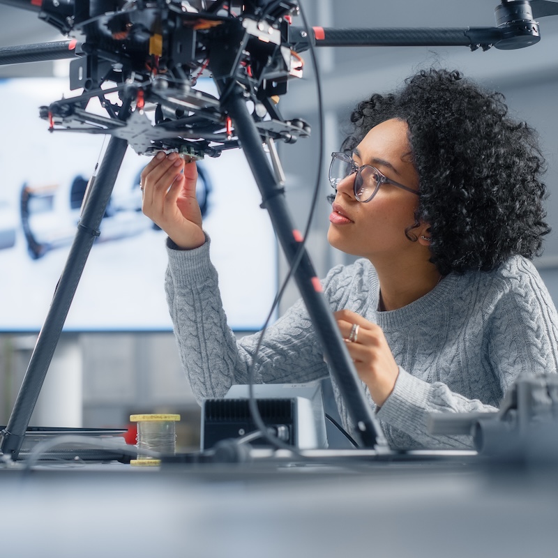 Eine junge Frau mit Brille arbeitet an der Unterseite eines kompliziert aussehenden technische Geräts.