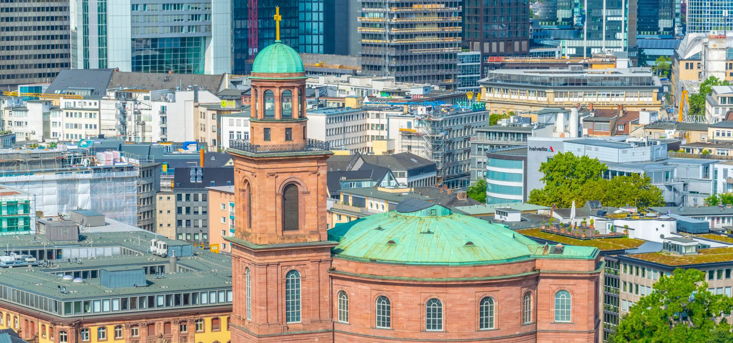 Zahlreiche Gebäudedächer auf einer dicht bebauten Fläche, teilweise mit Baustellengerüsten, im Hintergrund eine Skyline aus Hochhäusern mit vielen gläsernen Fronten.
