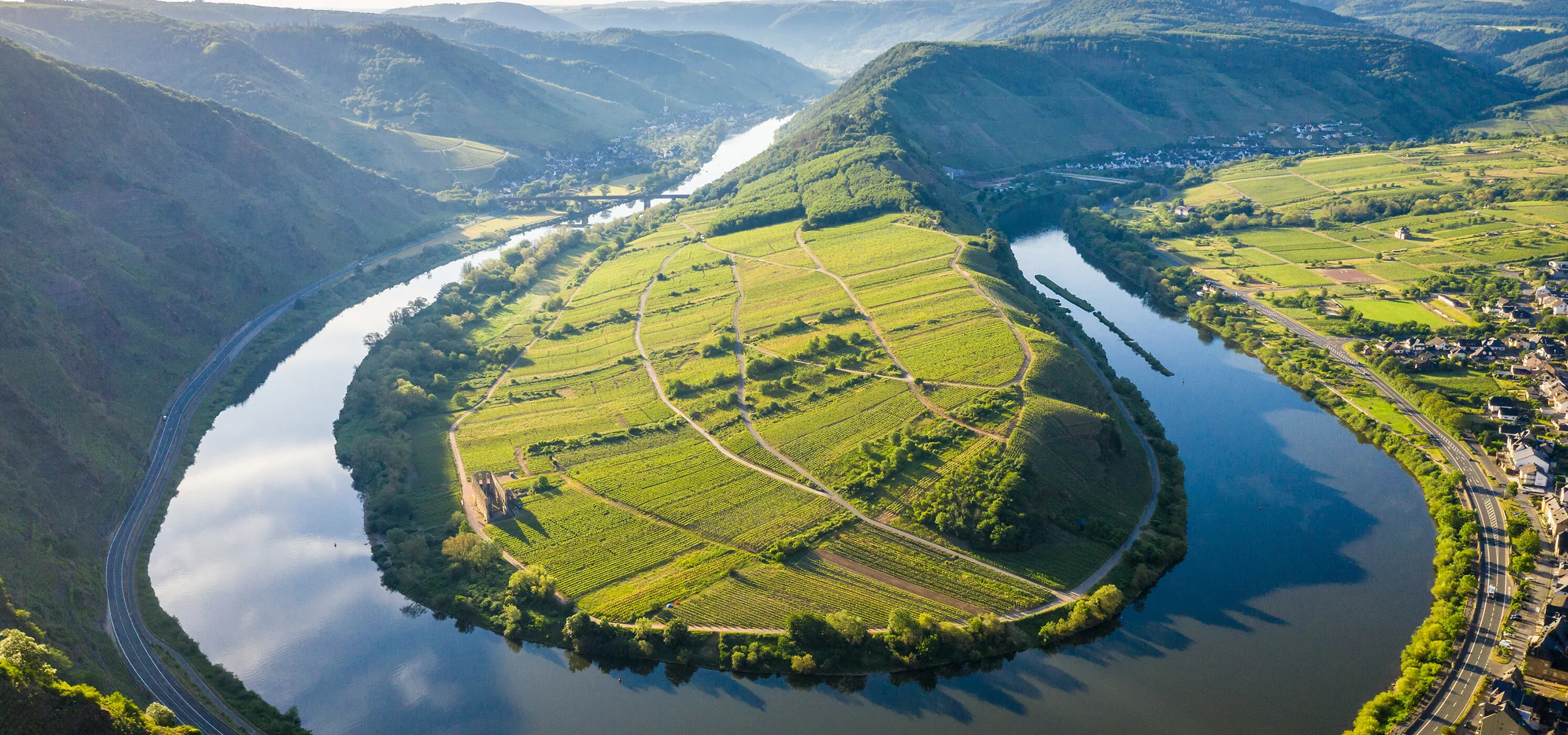 Ein Fluss in einer Biegung, darin eine hügelige Landzunge mit grünen Feldern.