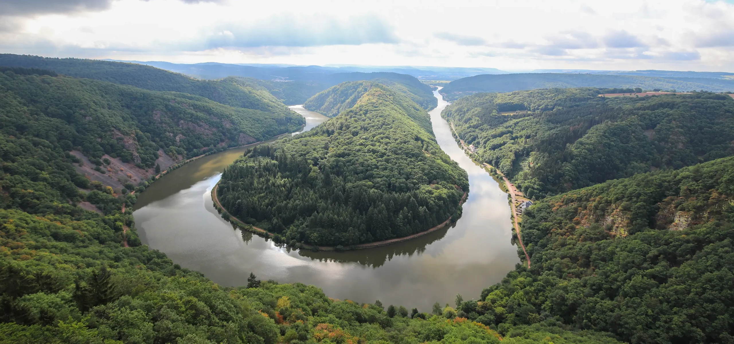 Eine Fluss umströmt einen saftig-grün bewaldeten Hügel.