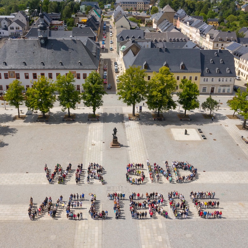 Aus der Luft sind Menschen zu sehen, die durch ihre Positionierung die Buchstaben für den Satz 'Wir sind Welterbe' bilden.