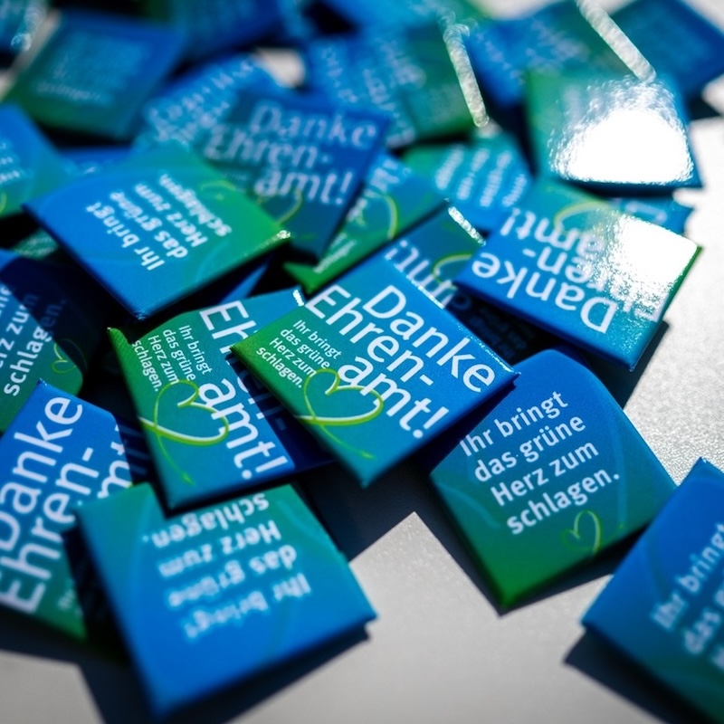 Ein Haufen blau-grüner Pins, deren Aufdruck 'Danke – Ehrenamt' zum Ausdruck bringen soll.