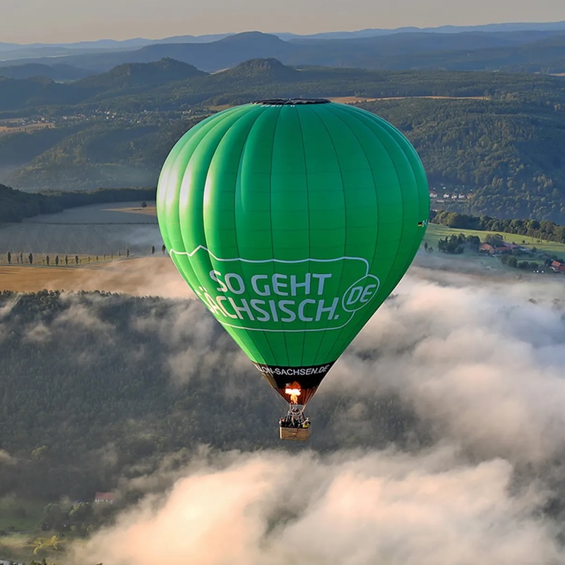 Ein grüner Heißluftballon oberhalb fluffiger Wolken.