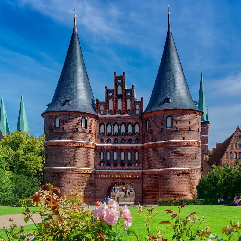 Das Holstentor in Lübeck. Ein Tor aus viel rotem Stein, links und rechts flankiert von zwei runden Türmen mit spitzen Dächern.