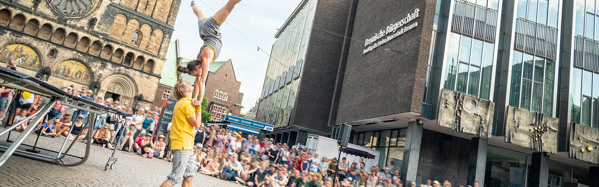 Zwei Artisten begeistern mit ihrer akrobatischen Show zwischen St. Petri Dom und dem Gebäude der Bürgerschaft zahlreiche Zuschauerinnen und Zuschauer.
