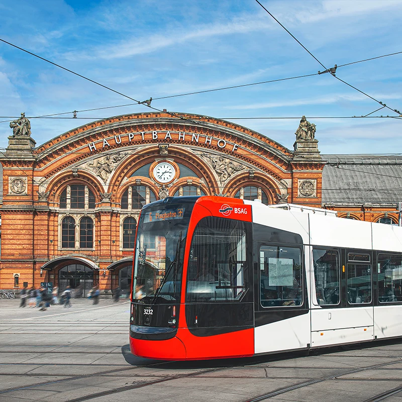 Eine Straßenbahn durchfährt eine Kurve, im Hintergrund der Bremer Hauptbahnhof.