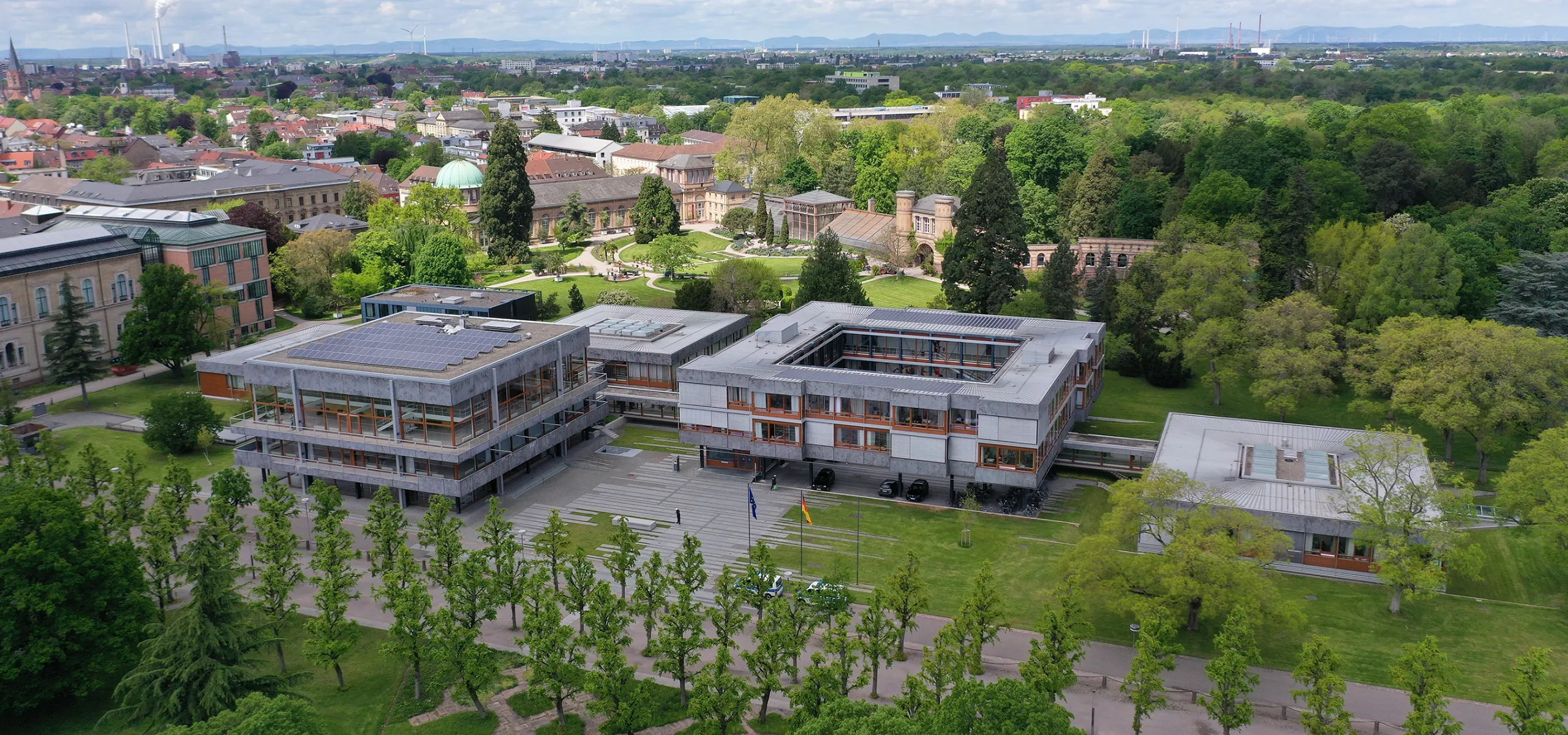 Ein mehrteiliges Gebäude aus grauem Beton und offenen Fensterflächen in einer grünen Umgebung.