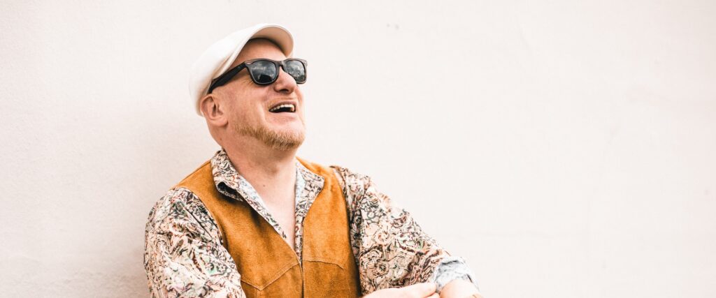 Flo Mega posiert lachend vor einer weißen Wand