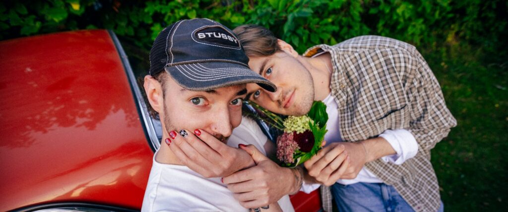 Die Mitglieder der Band Raum27 posieren mit Blumen vor einem roten Auto