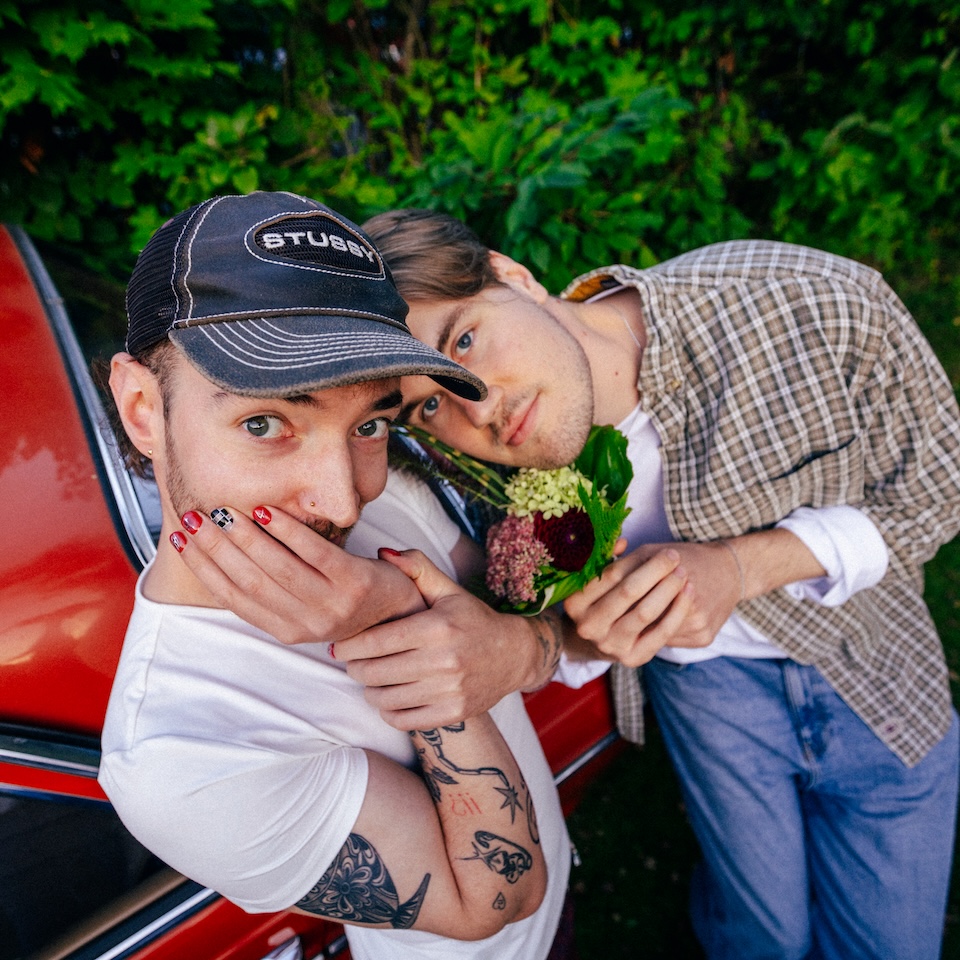 Die Mitglieder der Band Raum27 posieren mit Blumen vor einem roten Auto