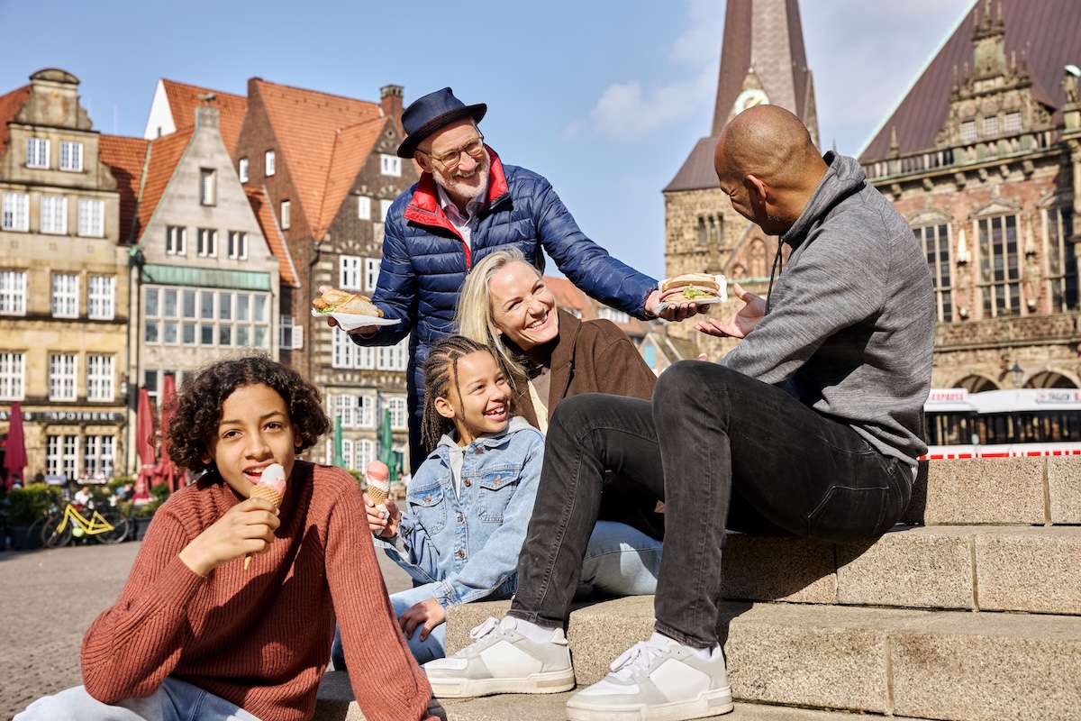 Fünf Personen sitzen am Bremer Marktplatz uns essen Fischbrötchen und Eis