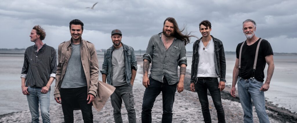 Die Mitglieder der Band Versengold posieren an einem Strand bei grauem Himmel