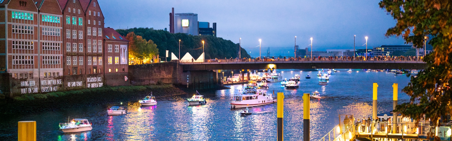 Viele leuchtende Schiffe treiben auf der Weser am Abend.