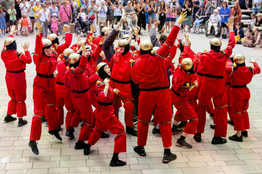 Eine in roten Overalls als Roboter verkleidete Tanzgruppe in Aktion.