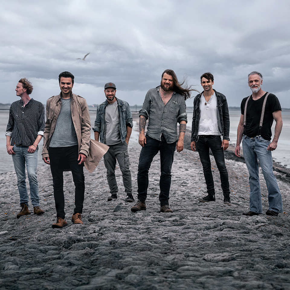 Die Mitglieder der Band Versengold posieren an einem Strand bei grauem Himmel