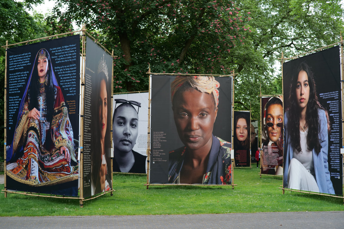 Große Plakate mit Portraitaufnahmen und Geschichten auf einer Rasenfläche.