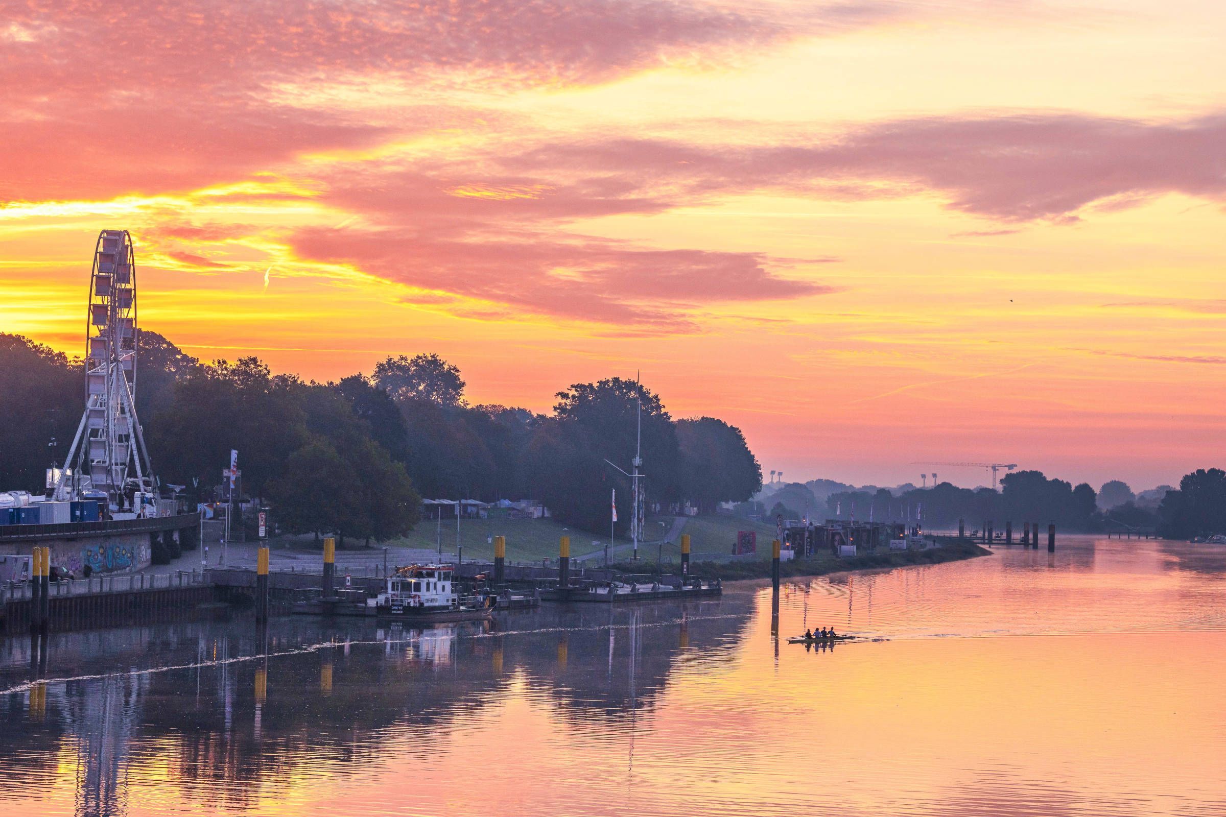 Ein Riesenrad auf einer Veranstaltungsfläche am Fluss im Morgenlicht.